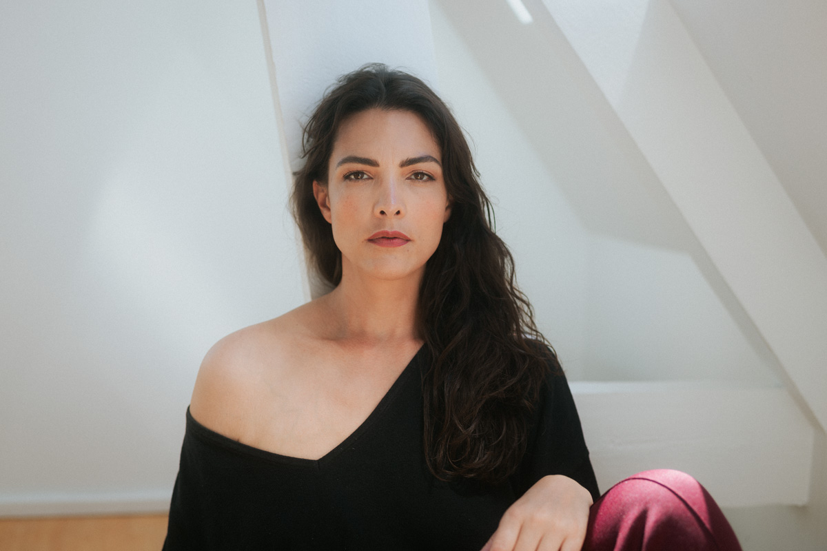 Caroline van der Leeuw zittend, kijkt ernstig in de camera.